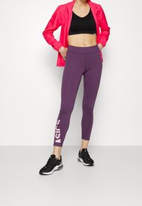 Sujetador deportivo negro, chaqueta rosa con cremallera y leggins morados con el logo blanco de "ASICS". Zapatillas deportivas negras con suelas ligeras. Textura de tela suave.