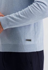Lichtblauw sweater gemaakt van zachte stof, met ribbelboorden en -zoom, met een klein zilveren logo-label aan de linkerkant.