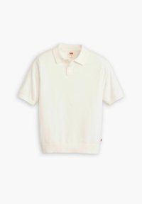 Polo à manches courtes blanc en coton. Il présente un col classique, une patte à trois boutons, ainsi que des poignets et un ourlet côtelés. Étiquette logo rouge en bas.