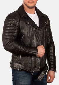 Zwarte leren jas met een gequiltde textuur en overlappende revers. Bevat zilveren ritssluitingen, een riem en gestructureerde accenten.
