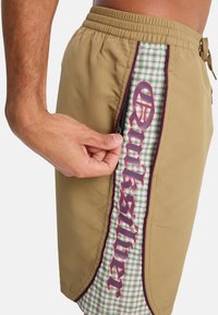 Μαγιό σορτς Quiksilver σε μπεζ χρώμα με πάνελ σε καρό μοτίβο. Διαθέτει τσέπη με φερμουάρ και αντίθετες μπορντό λεπτομέρειες στη πλευρά.