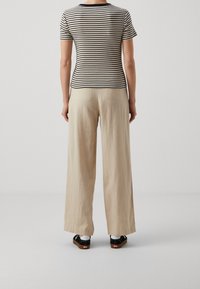 Haut à manches courtes rayé en crème et noir ; pantalon large beige décontracté ; associé à des chaussures noires et beiges. Tissu lisse avec une coupe décontractée.