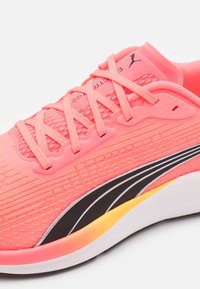 Zapatilla de Running con un upper de textil rosa, acentos negros y suela en degradado amarillo. Presenta una superficie texturizada y un diseño de cordones curvados.