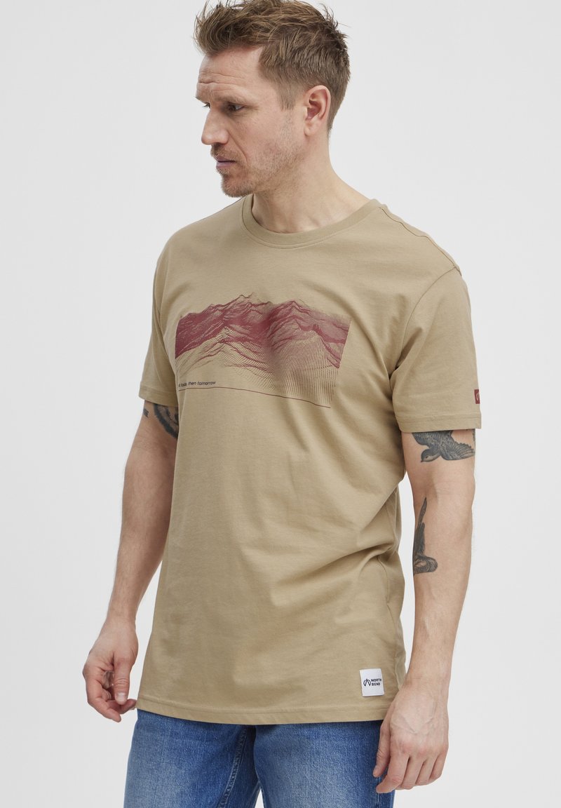 Bēšas kokvilnas t-krekls ar bordo kalnu grafiku pāri krūtīm un logotipa birku apakšmalā. Īsas piedurknes, apaļais kakls.