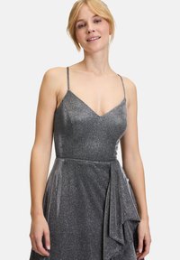 Graues Glitzerkleid mit dünnen Spaghettiträgern, einem V-Ausschnitt und einem gerafften Seitendetail. Der Stoff hat eine schimmernde Textur.