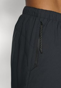 Sorte atletiske shorts med elastisk talje og en lynlåslomme i siden med en flettet pull-tab. Glat, letvægts stofstruktur.