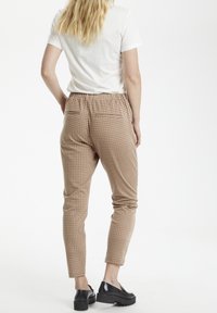 Bruna rutiga slim-fit byxor med elastisk midjeband och två bakfickor, i kombination med en vit t-shirt med kort ärm och svarta skor.