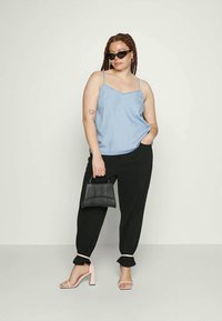 Top de camisolinha azul claro com alças finas, combinado com calças pretas ajustadas. Segurando uma pequena bolsa preta, calçando sandálias de salto bloco rosa.