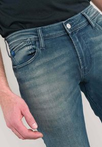 Vervaagde blauwe spijkerbroek met een recht model, vijf zakken en een zilveren knoop in de taille. Licht textuur met subtiele stikseldetails.