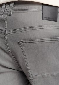 Grijze denim jeans met een gladde textuur, voorzien van contrasterende stiksels, een achterzak en een zwart leren merklabel dat geperst is met "NO EXCESS."