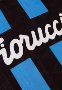 Zwarte textiel met geprofileerde blauwe strepen en witte "Fiorucci" branding. Gladde textuur; geometrisch patroon zichtbaar op de achtergrond.