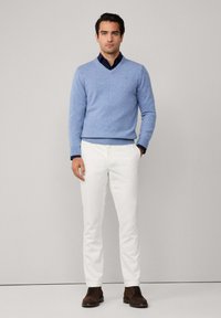 Světlemodrý svetr s výstřihem do V v kombinaci s tmavě modrou košilí, bílými kalhotami a hnědými šněrovacími botami. Hladká textura, dobře padnoucí střih, pohodlný design.