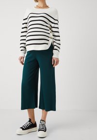 Strikket sweater i hvid og sort med knapdetaljer, parret med teal bredbenede ribbede bukser og sorte sneakers med hvide såler.