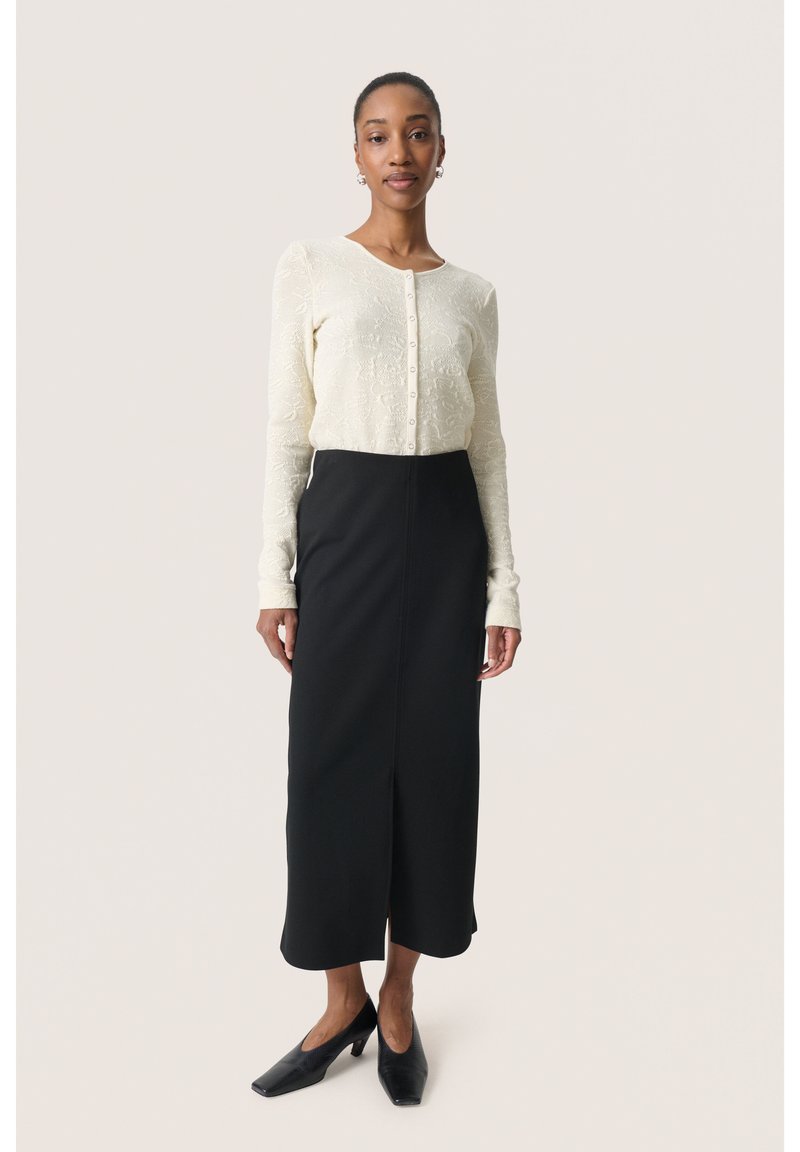 Hvid blonde bluse med lange ærmer og knaplukning, parret med en sort midi-nederdel. Sorte højhælede sko. Enkel, elegant design.