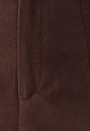 Brauner Stoff mit strukturierter Webart, ausgestattet mit einer Seitentasche und sichtbaren Nahtdetails. Die Oberfläche wirkt leicht grob.