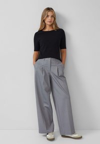 Top corto a maniche corte nero a coste abbinato a pantaloni larghi grigi a righe. I pantaloni presentano delle pince e una chiusura con bottone. Scarpe casual completano il look.