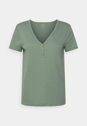 T-shirt vert sauge à manches courtes, côtelé avec un col en V et quatre petits boutons au centre devant, présenté sur un fond uni.