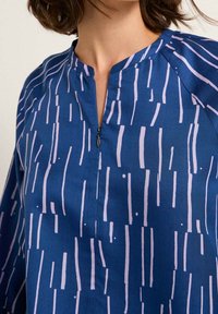 Marineblå bluse med lodrette pink striber og prikker, med en lille lynlås foran og en notchet halsudskæring. Letvægtsstof med en glat tekstur.