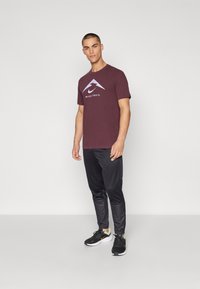 T-shirt de manga curta cor vinho com logótipo, combinada com calças pretas afuniladas e ténis pretos. Design simples com textura suave.