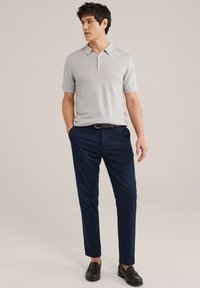 Gai pelēks īsām piedurknēm polo krekls ar trim pogām, apvienots ar tumši zilām biksēm un melniem loafers. Vienkāršs, pielāgots dizains.