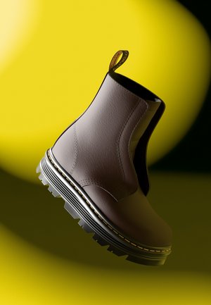 Bottine en cuir marron avec des panneaux latéraux élastiques, une surface texturée et une semelle en caoutchouc noir épaisse avec des accents de couture jaune.