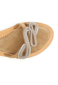 Beige mokkasiinisandaalit, joissa on pehmeä pohja, koristeellinen hopeinen helminauha silmukkakuviolla ja sileä ruskea ulkopohja.
