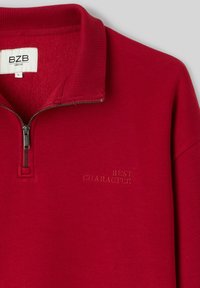 Sweat-shirt à col demi-fermeture éclair rouge, col côtelé, avec "BEST CHARACTER" brodé sur le côté gauche de la poitrine. Texture de tissu doux.