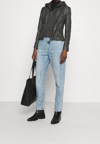 Zwarte leren motorjack over een grijze hoodie met ritssluiting, lichtblauwe tapering jeans, zwarte enkelboots, met een zwarte tote bag.