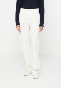 Biele nohavice s širokými nohavicami a vysokým pásom, vyrobené z hladkej látky, s predným zapínaním na gombíky a bočnými vreckami. Nosia sa s bielou obuvou.