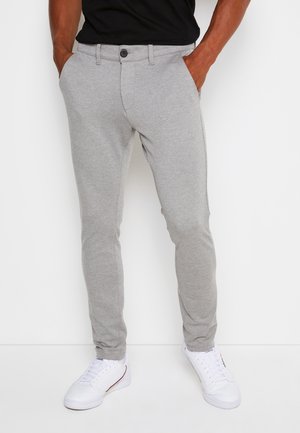 Hellgraue, slim-fit Hosen aus weichem Stoff mit glatter Textur, ausgestattet mit einem Knopfverschluss und Seitentaschen. Kombiniert mit weißen Sneakern.