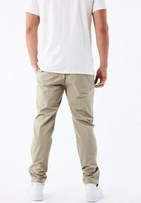Pantalones ligeros beige con un corte holgado, que presentan bolsillos laterales y una textura suave. Combinados con una camiseta blanca sencilla y zapatillas blancas.