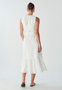 White midi dress with a tiered hem and relaxed fit, featuring a keyhole back detail and elastic waist. Smooth fabric and simple design.