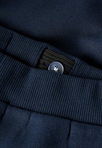 Marineblå bomullsblandete bukser med ribbestrikket midjebånd, som har en knappedetalj og subtil tekstur. Nærbilde som fremhever stoff og passform.