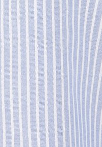 Tessuto a righe in blu chiaro e bianco. Presenta sottili righe verticali con una trama testurizzata, creando un sottile effetto dimensionale.