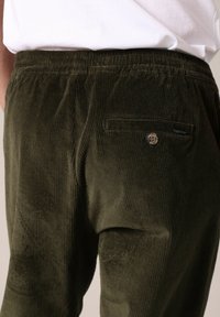 Donkergroene corduroy broek met een textuur op het oppervlak, voorzien van een achterzak en een knoopdetail. Elastische tailleband voor comfort.