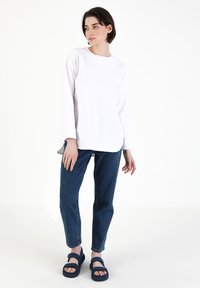 Hvid langærmet top med rund halsudskæring, kombineret med medium blå jeans og marineblå sandaler med dobbelte stropper og strukturerede såler.