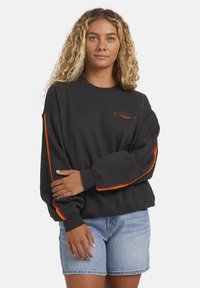 Sudadera negra con detalles de rayas rojas y amarillas en las mangas, con un pequeño logo bordado en el pecho y un diseño de corte relajado.