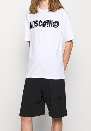 Weißes T-Shirt mit fettgedrucktem schwarzem Schriftzug "MOSCHINO" und schwarze Shorts mit Logodruck, beide aus weichem Stoff, geeignet für lässige Freizeitkleidung.