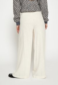 Kremne široke hlače iz lahkega teksturiranega materiala. Opremljene so z visokim pasom in rahlim nabiranjem. V kombinaciji z vzorčastim puloverjem.