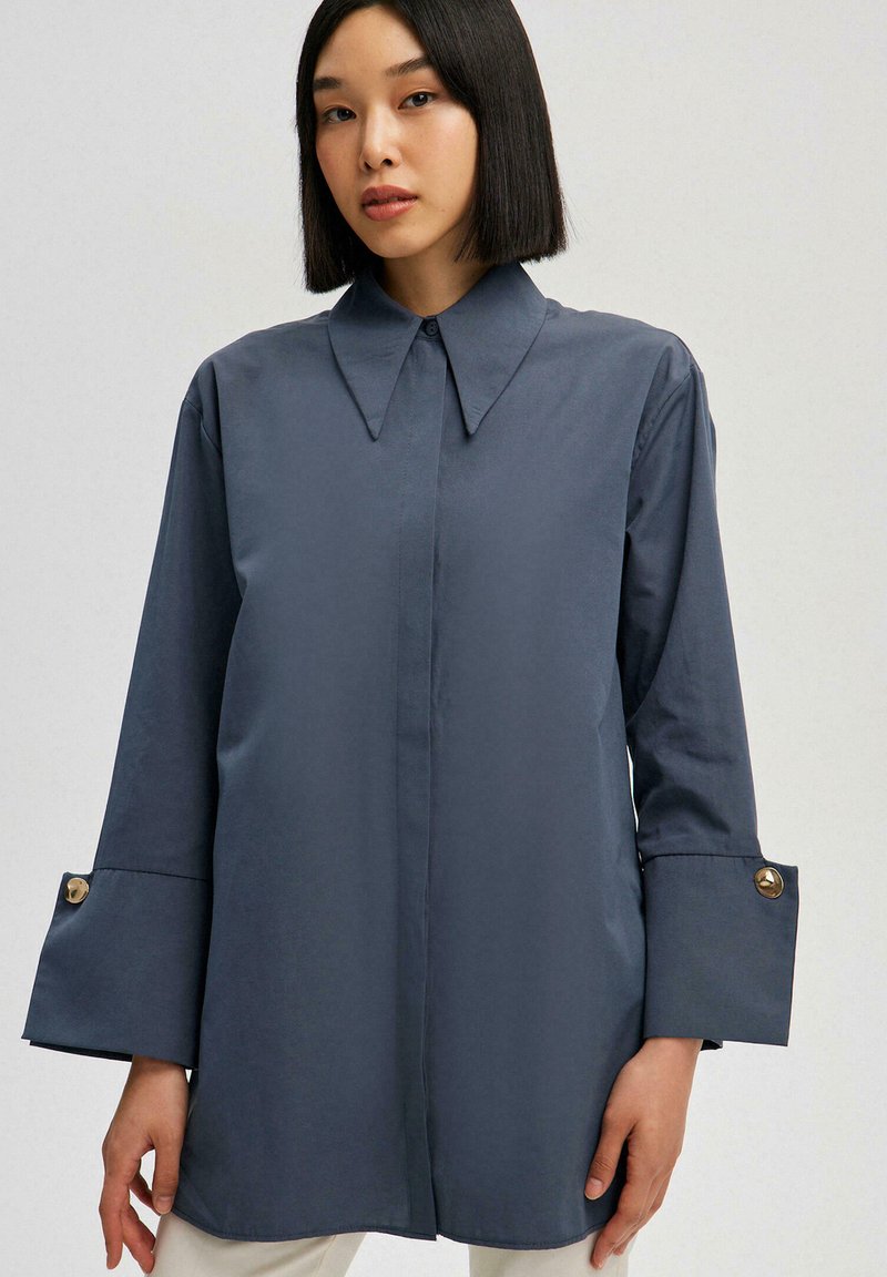 Navy blue long-sleeve shirt with a sharp collar, gold button accents on wide cuffs, and a smooth cotton texture.