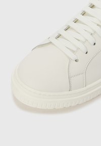 Baskets en cuir blanc avec bout rond, lacets plats blancs, coutures renforcées et semelle en caoutchouc texturée. Finition lisse et détails minimalistes.