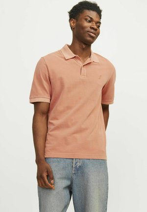 Camisa polo de color rosa claro con cuello y mangas cortas, hecha de algodón texturizado, combinada con unos vaqueros de color azul claro. Pequeño logo en el pecho.