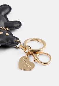 Llavero de cuero negro en forma de oso con herrajes dorados, con una etiqueta en forma de corazón grabada con "TWINSET MILANO."