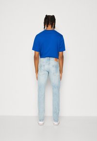 Jasnoniebieskie jeansy denim o prostym kroju nogawek, zestawione z intensywnie niebieskim bawełnianym t-shirtem. Na tylnej części znajduje się beżowa skórzana metka z logo marki.