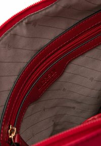 Rotes Stoffinnenfach einer Handtasche mit einem Reißverschlusstaschenfach und glattem braunem Futter mit dezentem Muster. Reißverschlussbesatz in Schwarz.