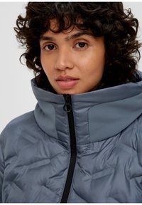 Gepolsterte graue Jacke mit hohem Kragen, ausgestattet mit einem Reißverschluss und Bereichen aus strukturiertem Stoff für Isolierung und Stil.