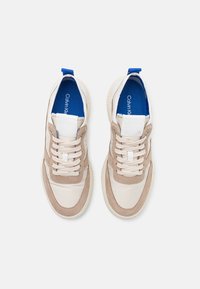 Baskets avec une tige en daim beige et cuir crème, des accents beige clair, une semelle intérieure bleue et des lacets blancs. Bout rond et semelle texturée.