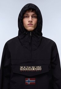 Giacca nera con cappuccio, chiusura frontale con zip e una grande tasca. Presenta un logo ricamato e una bandiera della Norvegia. Materiale leggero e texturizzato.