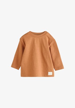 Hosszú ujjú ing puha, rozsdabarna szövetből. Kerek nyakkivágással és vállnál patentokkal rendelkezik, az alján pedig egy kis címke található.