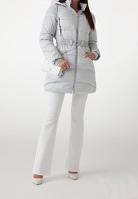 Grå dunjakke med hætte, tekstureret mønster, indsnævret talje og lynlås-lukning. Sat sammen med hvide udvidede bukser og cremefarvede hæle.